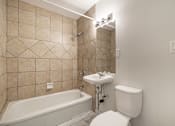 Thumbnail 129 of 219 - A white toilet sits next to a bathtub in a bathroom with beige tiled walls.