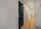 Thumbnail 100 of 219 - A long hallway with a black door on the left and a wooden floor.