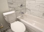 Thumbnail 83 of 219 - A white toilet sits next to a bathtub in a bathroom with marble tile walls.