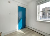 Thumbnail 158 of 219 - A room with a blue door and a window showing a city view.