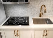 Thumbnail 141 of 219 - A kitchen with a black stove top and a sink with a gold faucet.