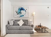 Thumbnail 161 of 219 - A grey couch with a white pillow and a blue painting on the wall.
