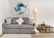 Thumbnail 160 of 219 - A grey couch with a white pillow and a blue painting on the wall.