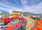 Thumbnail 17 of 27 - A wooden deck with red and black furniture and a fire pit.