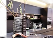 Thumbnail 6 of 11 - A tall vase with a plant in it is on a counter.