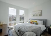 Thumbnail 24 of 66 - Modern bedroom at The Rail Bound Brook with three large windows, city views, and a cozy bed—offering comfort and elegance in NJ apartment living.