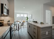 Thumbnail 16 of 66 - Open concept kitchen and living room at The Rail Bound Brook with wood-style flooring, stainless steel appliances, and large sunlit windows.