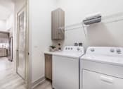 Thumbnail 12 of 18 - a utility room with a washer and dryer and a kitchen in the background