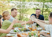 Thumbnail 5 of 17 - A group of people toasting with drinks at a dinner table.