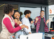 Thumbnail 6 of 17 - Four people are standing in front of a grill, smiling and laughing together.