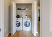 Thumbnail 30 of 98 - A laundry room with two washing machines and a shelf with towels and a plant.