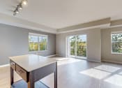 Thumbnail 40 of 98 - A spacious room with a table and chairs in the foreground and sliding glass doors leading to a balcony.