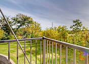 Thumbnail 44 of 98 - A balcony with a metal railing overlooks a green lawn and trees.