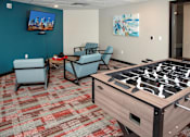 Thumbnail 74 of 98 - A foosball table is in the middle of a room with two chairs and a television.