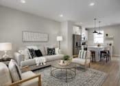 Thumbnail 6 of 16 - A modern living room with a grey sofa, a coffee table, and a dining area in the background.