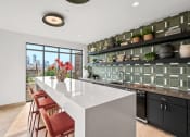 Thumbnail 23 of 63 - Community rooom kitchen with a white counter top and a large island with red chairs