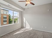 Thumbnail 35 of 39 - A room with a ceiling fan and a window overlooking a building.