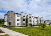 Thumbnail 2 of 6 - Apartment complex with grey and white buildings and green lawns.