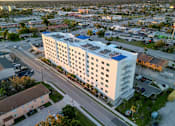 Thumbnail 1 of 13 - A large white building with a blue roof is surrounded by a parking lot and other buildings.