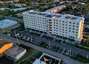 Thumbnail 4 of 13 - A large white hotel with a parking lot in front.