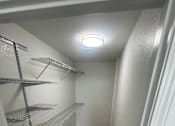 Thumbnail 15 of 22 - A long, narrow walk-in closet with shelving and a light on the ceiling.