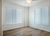 Thumbnail 9 of 30 - A room with wooden floors and two windows covered with blinds.