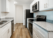 Thumbnail 7 of 30 - A kitchen with white cabinets and a black refrigerator.