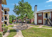 Thumbnail 7 of 35 - A tree in a grassy area in front of apartment buildings.