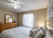 Thumbnail 23 of 35 - A bedroom with a bed, dresser, mirror, and a ceiling fan.