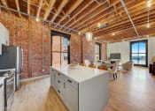Thumbnail 16 of 41 - a kitchen and living room with exposed brick walls and a white counter top at Greeley Lofts, St. Louis, MO, 63102