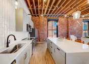Thumbnail 15 of 41 - a kitchen with a large white counter top and a exposed brick wall at Greeley Lofts, St. Louis, MO, 63102