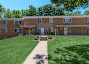 Thumbnail 18 of 23 - a brick apartment building with a green lawn and trees in the background