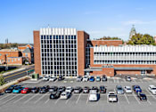 Thumbnail 54 of 61 - A parking lot in front of a large building with a glass facade.