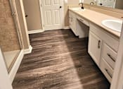 Thumbnail 16 of 27 - A bathroom with a white door, sink, and brown flooring.