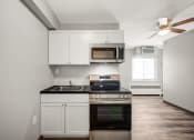 Thumbnail 16 of 48 - a kitchen with white cabinets and black appliances and a ceiling fan