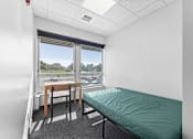 Thumbnail 17 of 61 - A room with a bed, table and chairs with a window overlooking a parking lot.