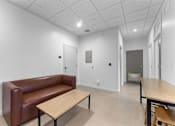 Thumbnail 21 of 61 - A brown leather couch sits in a white room with a wooden table in front of it.