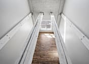 Thumbnail 25 of 58 - A long wooden staircase with metal handrails on both sides leading to a bright light at the top.