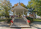 Thumbnail 59 of 61 - A gazebo with a red bow is surrounded by trees.