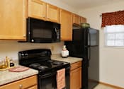 Thumbnail 3 of 13 - A black refrigerator sits in a kitchen with wooden cabinets.