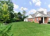 Thumbnail 4 of 27 - A house with a red brick exterior and a white roof is surrounded by a green lawn and trees.