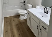 Thumbnail 17 of 18 - A white toilet is in a bathroom with wood floors.