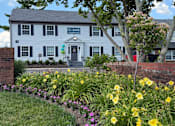 Thumbnail 1 of 18 - A white building with a grey roof and a garden in front.