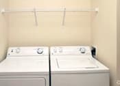 Thumbnail 12 of 15 - Two white front loading washing machines in a laundry room.