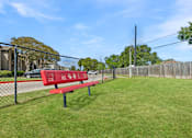 Thumbnail 13 of 23 - A red bench sits in a grassy area next to a fence.