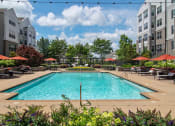 Thumbnail 8 of 40 - a swimming pool with lounge chairs and umbrellas in front of an apartment building at Emblem Alpharetta, Alpharetta, 30009