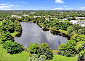 Thumbnail 36 of 38 - A lake surrounded by green trees and buildings in the distance.
