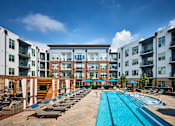 Thumbnail 14 of 39 - A large swimming pool surrounded by sun loungers and umbrellas in front of apartment buildings.