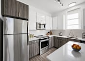 Thumbnail 26 of 27 - A modern kitchen with a stainless steel refrigerator and a bowl of oranges on the counter.
