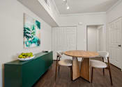 Thumbnail 8 of 26 - A green cabinet with a bowl of fruit on top and a painting of green leaves on the wall.